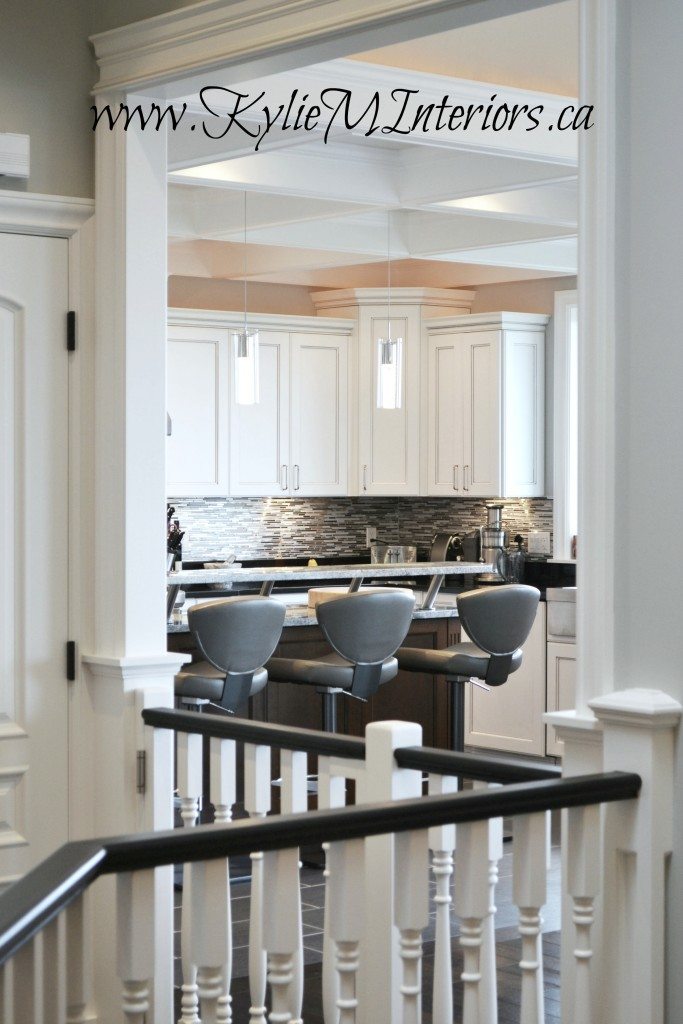 View from stairwell with black railing into the white kitchen with coffered ceilings