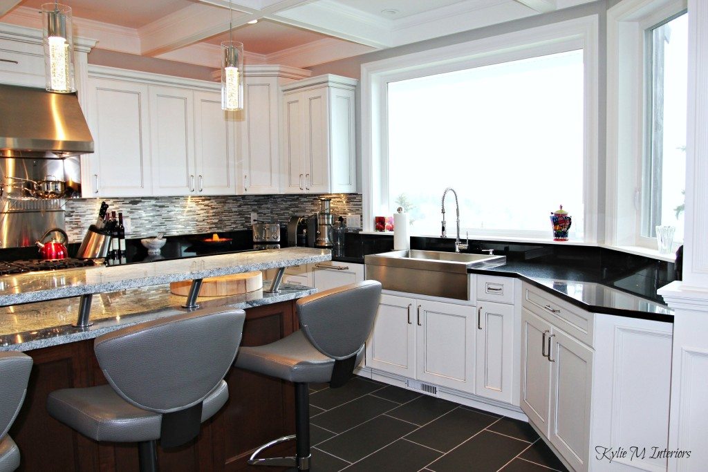 White kitchen with large windows, marble island countertops, black granite and stainless apron front sink