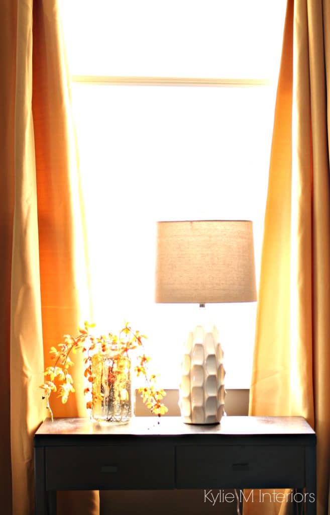 Home decor in south facing bedroom with dark brown, gold, yellow accents. Table lamps and dark wood side table with drapes