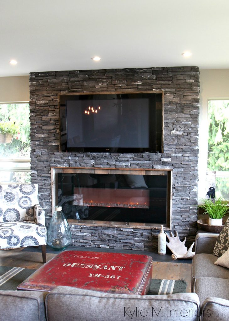 Rustic ledgestone fireplace with reclaimed wood surround and TV on top. Hunting inspired decor with gray sectional by Kylie M Interiors