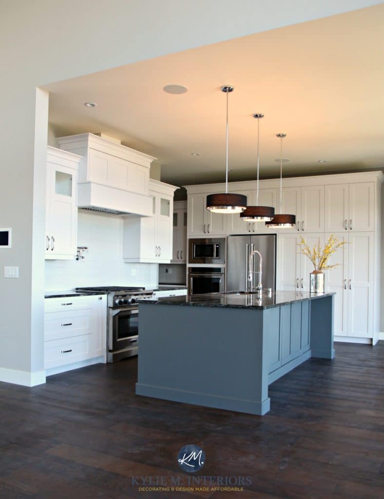 Open layout kitchen with white cabinets, gray island, Cambria Quartz Ellesmere countertop, black pendants and dark wood flooring. Kylie M Interiors