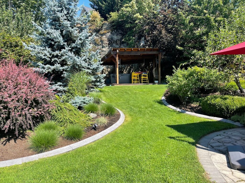backyard exterior update with concrete curbing between grass and landscape beds, garden beds, annuals, evergreens, perenials, hottub gazebo.