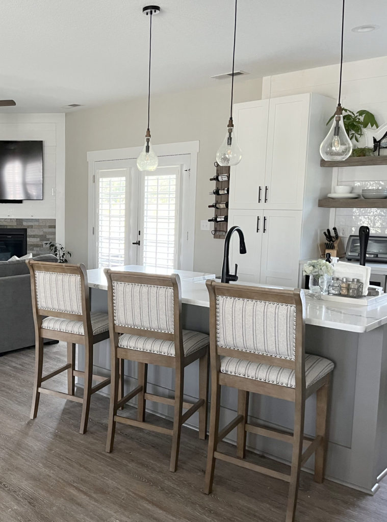 Sherwin Williams Agreeable Gray best greige warm gray paint colour, wood laminate gray wash floor, corner fireplace, white kitchen cabinets, Dovetail island.