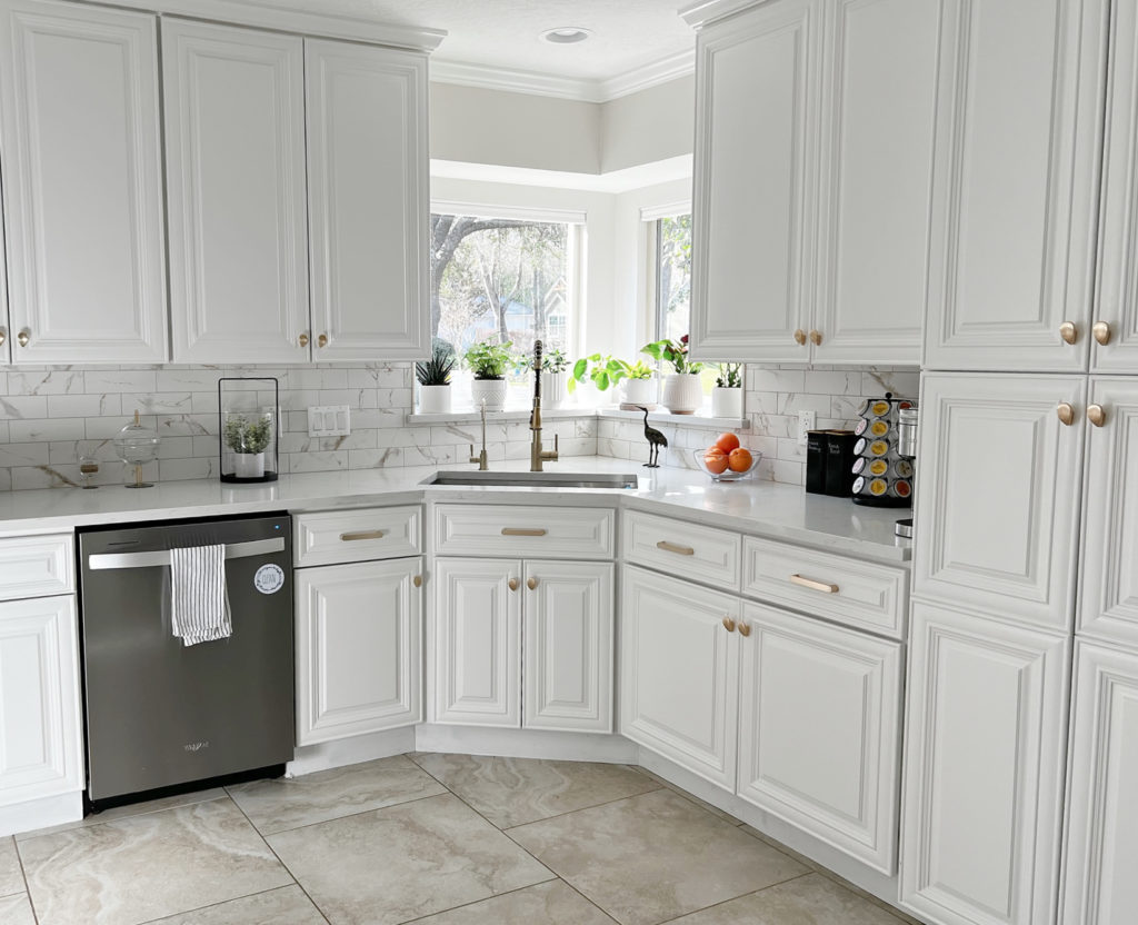 Sherwin Williams Pure White painted kitchen cabinets, paint color on walls, Benjamin Moore Collingwood. Soft white quartz countertop, gray veining, marble look backsplash, gold hardware. Kylie M.