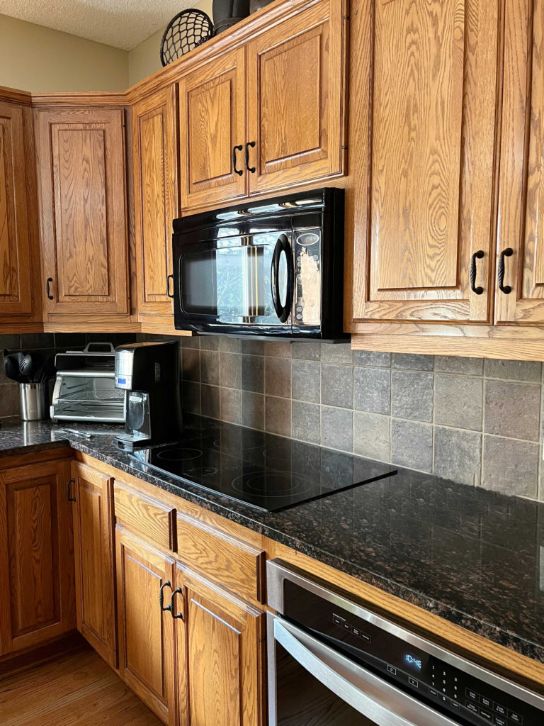 Oak cabinets with black granite countertop, tile backsplash, black appliances.