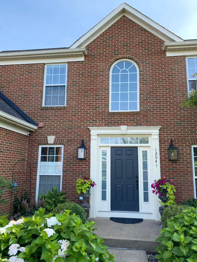 Exterior of home with red brick, white cream trim, no shutters and Benjamin Moore dark navy blue Cheating Heart front door, lighting. Kylie M Interiors Edesign, online paint color consultant