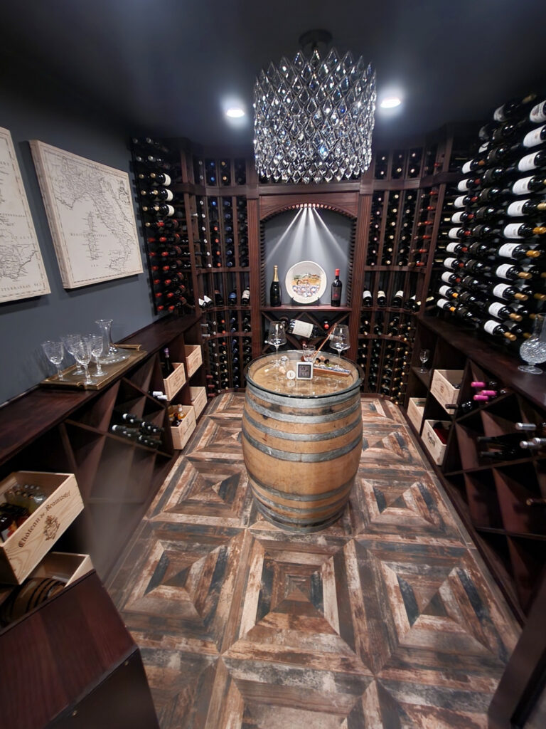 Wine room with wood floor, barrel, built in red cherry wood stained wine racks, crystal chandelier, Benjamin Moore Charcoal Slate, blue gray paint color on walls and ceiling. Kylie M Edes