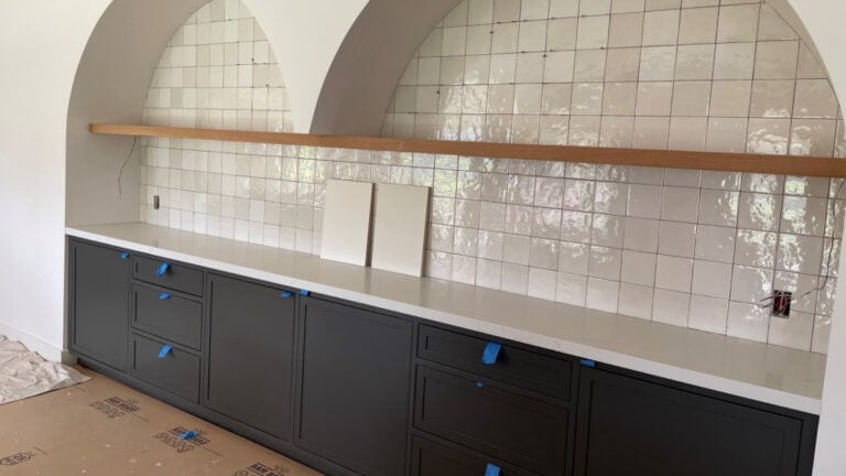 Home bar built-in with zellige tile, arches, floating wood oak shelf, and Sherwin Williams Iron Ore cabinets.