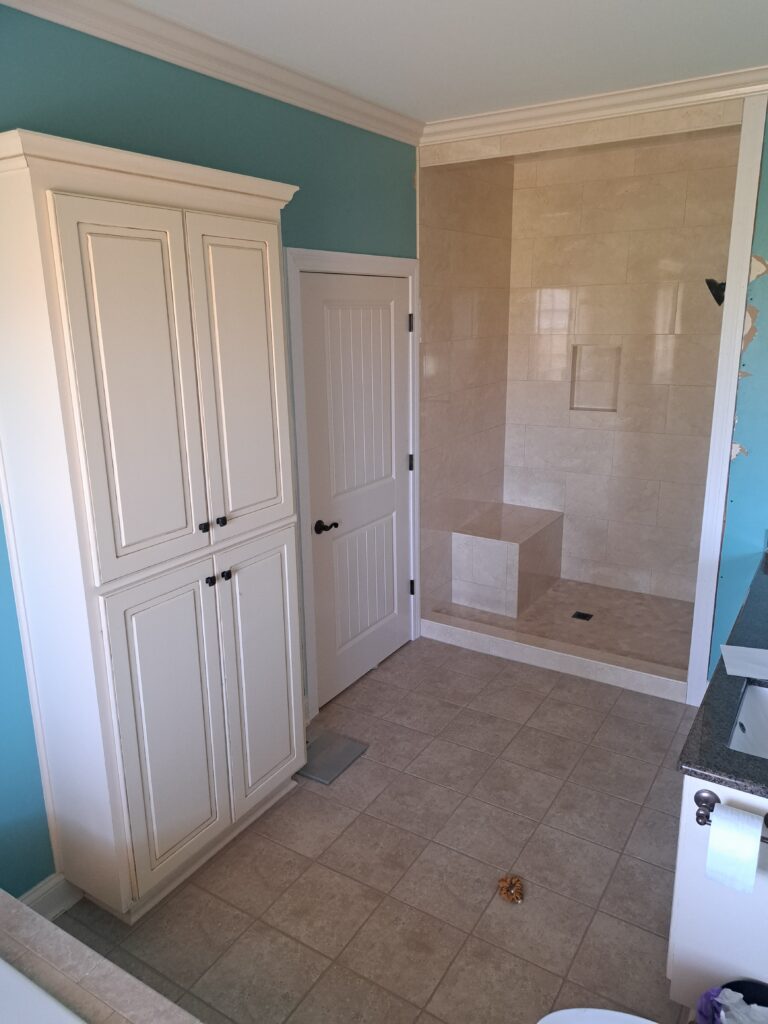 Bathroom update beige travertine tile in shower and tile floor with teal walls and cream trim.