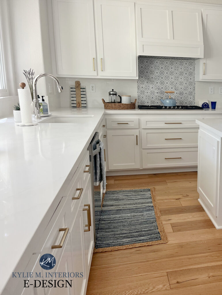 Sherwin Williams Pure White best white kitchen cabinet color. Wood floor. White quartz marble look countertop, tile behind stove. Gold hardware. Kylie M Edesign