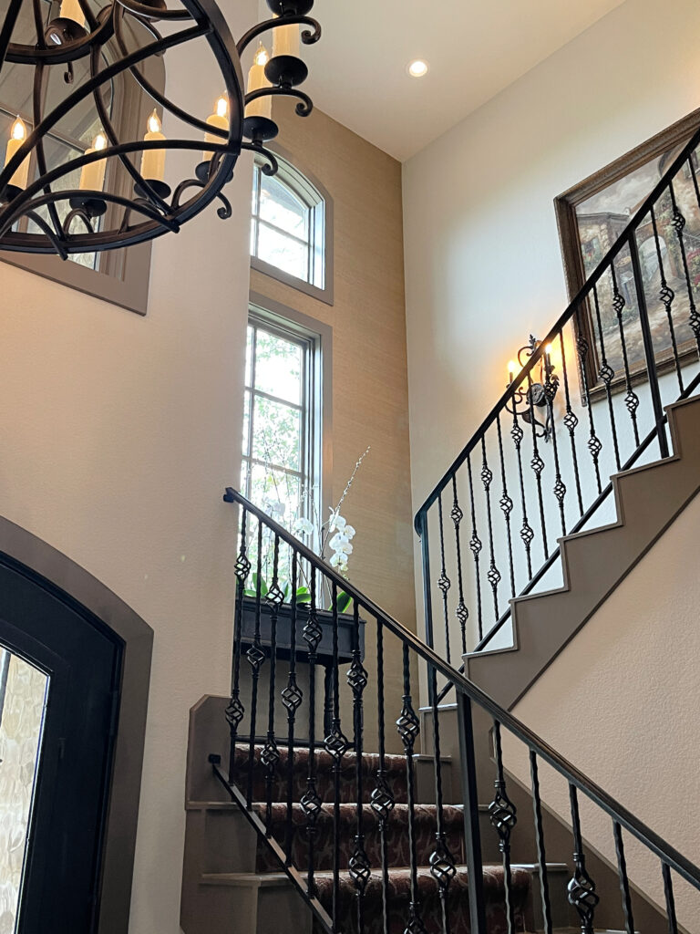 Spanish or tuscan style entrywy and staircase, iron railings and chandelier, off-white beige walls, Aesthetic White, Greige painted trim (warm gray). Kylie M ONline paint color expert