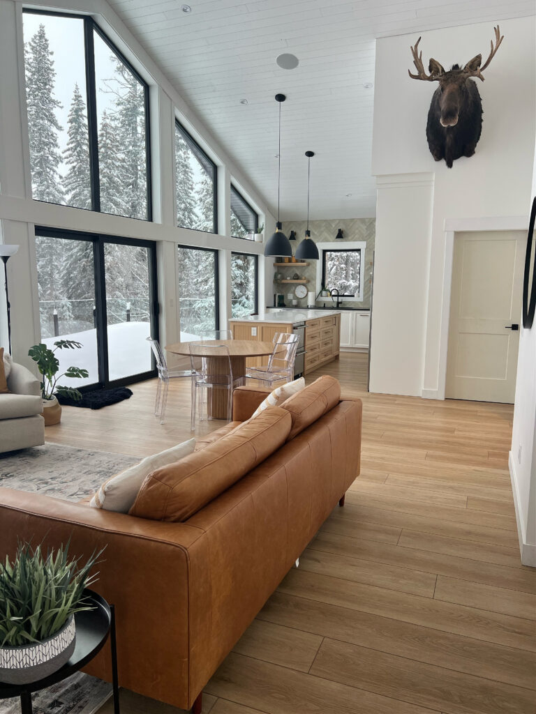 Mountain home, ski chalet style with BEnjamin Moore Oxford White, cognac leather sofa, wood floor, taxidermy, mounted moose, black windows, vaulted tongue and groove ceiling
