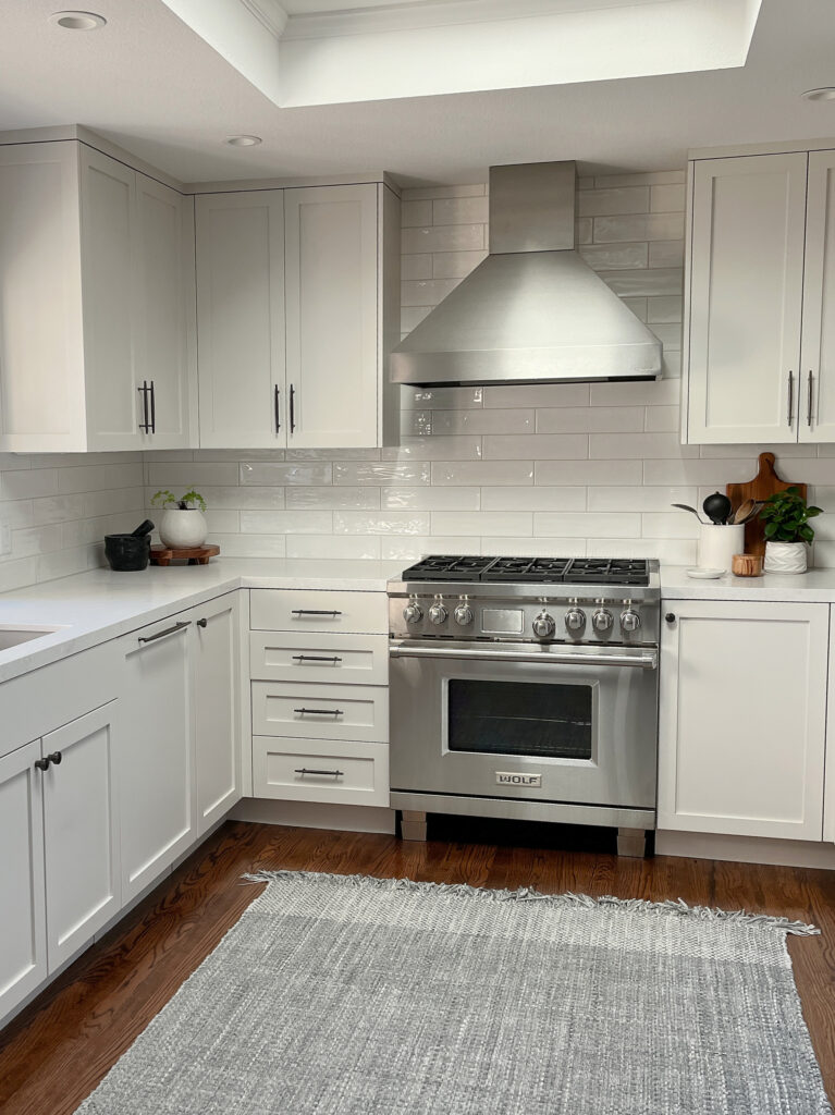 Off-white warm gray painted kitchen cabinets, Sherwin Williams Eider White with light gray quartz, stainless steel and subway tile