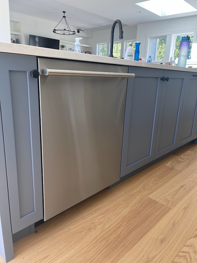 Benjamin Moore Britannia Blue on painted lower cabinets and island with off-white quartz, white oak wood floor and stainless steel appliances.