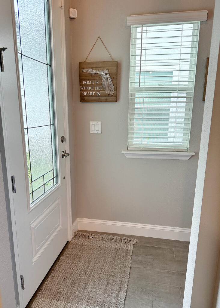 Entryway foyer with Behr Gratifying Gray warm neutral paint color, Extra White trim, white fronty door and wood look tile floor.