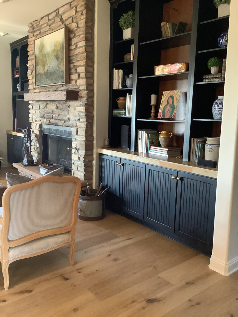 Living room built in cabinets painted wood in black, stone fireplace with wood floor, wood mantel. Kylie M Online paint color expert, client photo