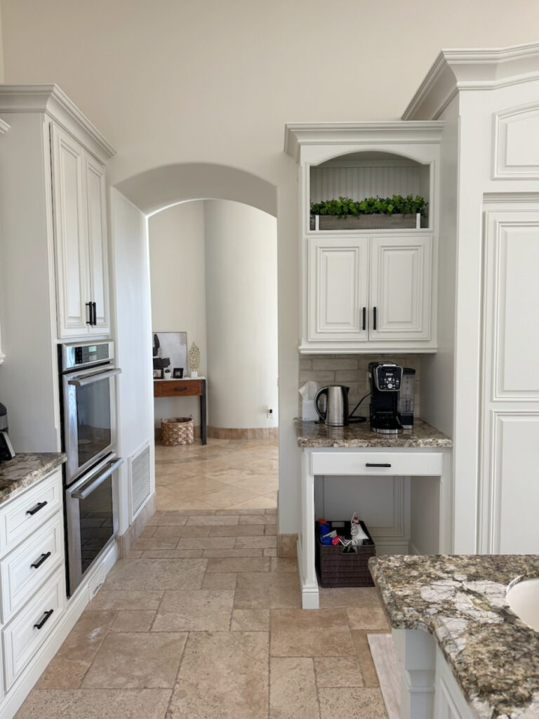 Travertine tile floor with Benjamin Moore Dove Wing, off white paint color, arched opening, painted cabinets, tuscan style kitchen