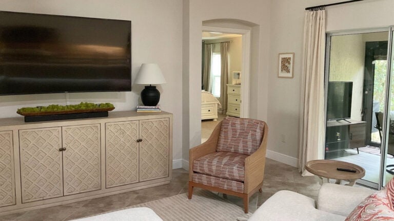 Living room with cabinet below wall mount TV, accent chair with red, neutral warm walls