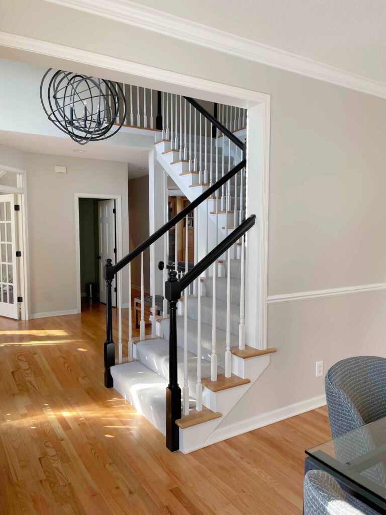 Benjamin MOore Edgecomb Gray in staircase and foyer, warm wood oak floor, painted black handrailing, wood steps, white spindles, carpet on stairs