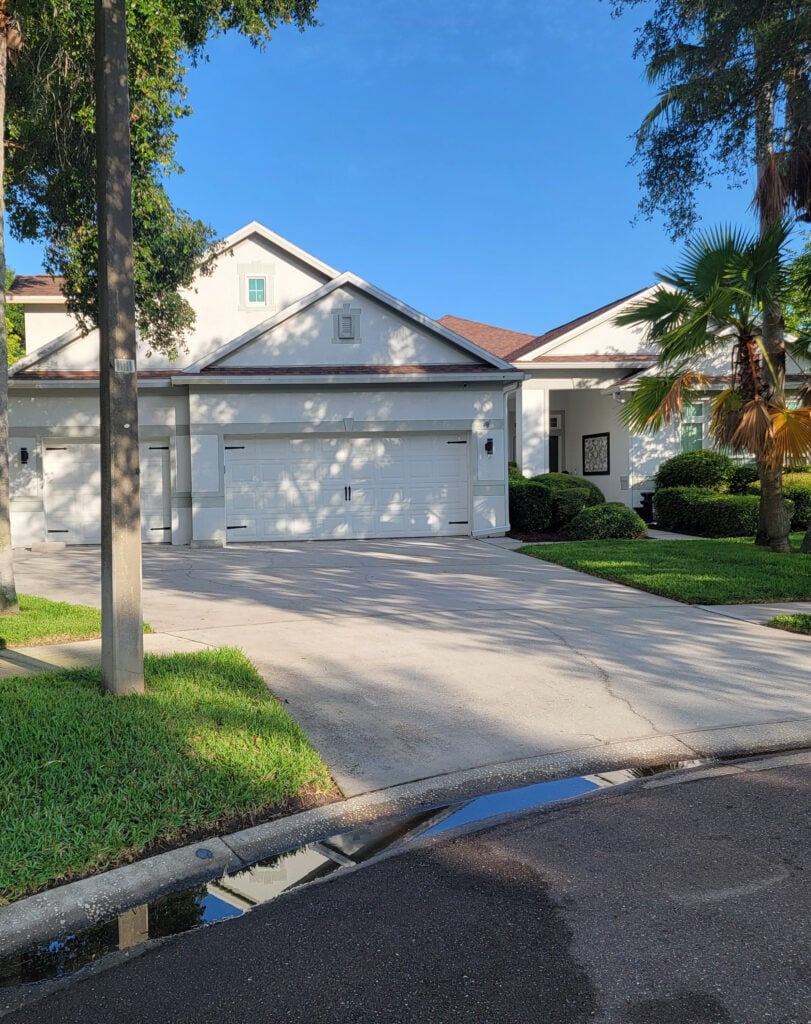 Florida-style exterior with asphalt roof (orange-brown-purple tones), painted off-whit stucco, white windows