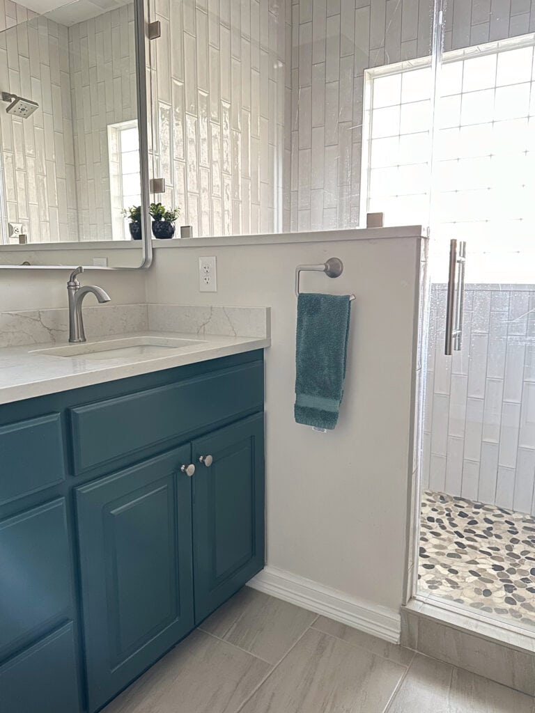 Oak wood vanity in bathroom painted Sherwin Williams Riverway, marble-look tile floor, off-white quartz countertop, shower tile subway tile