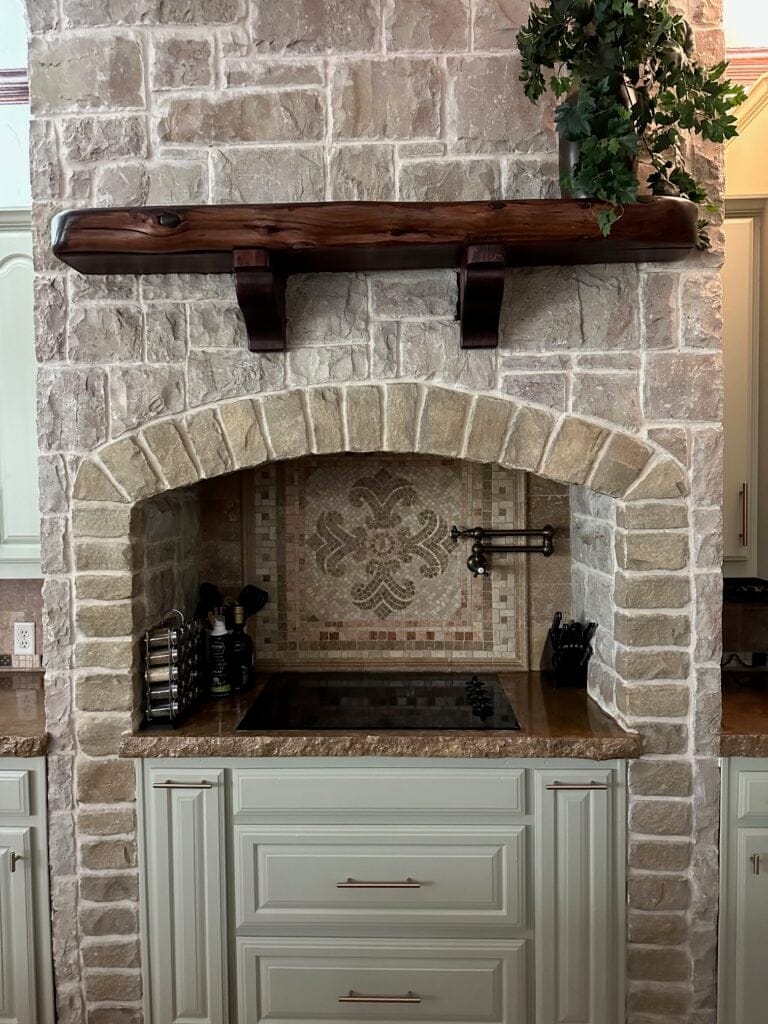 Sherwin Williams Grassland painted green cabinets with warm gray and taupe stone around the cooktop. Travertine tile backsplash.