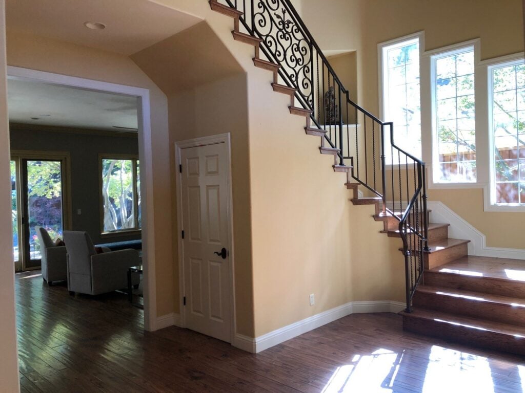 uscan style staircase, dark wood floor, scroll style metal hand railing on stairs, gold paint color on walls before edesign