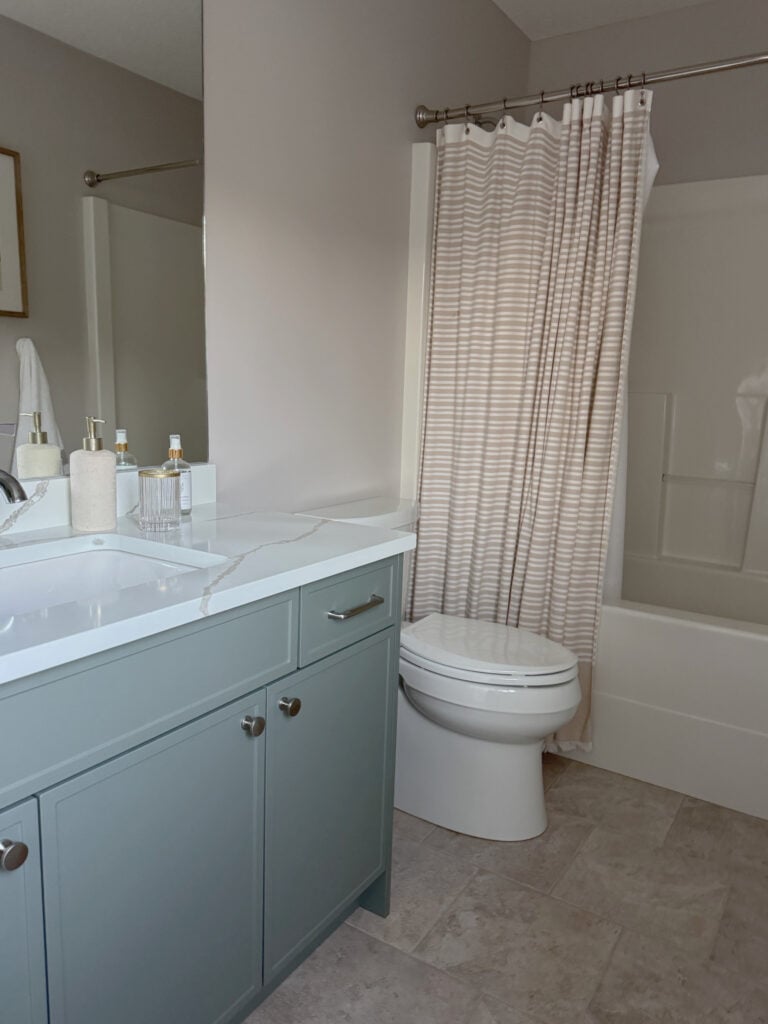 Sherwin Williams Pediment in bathroom with off-white shower surround, white quartz countertop and sage green bathroom vanity cabinet with beige tile floor