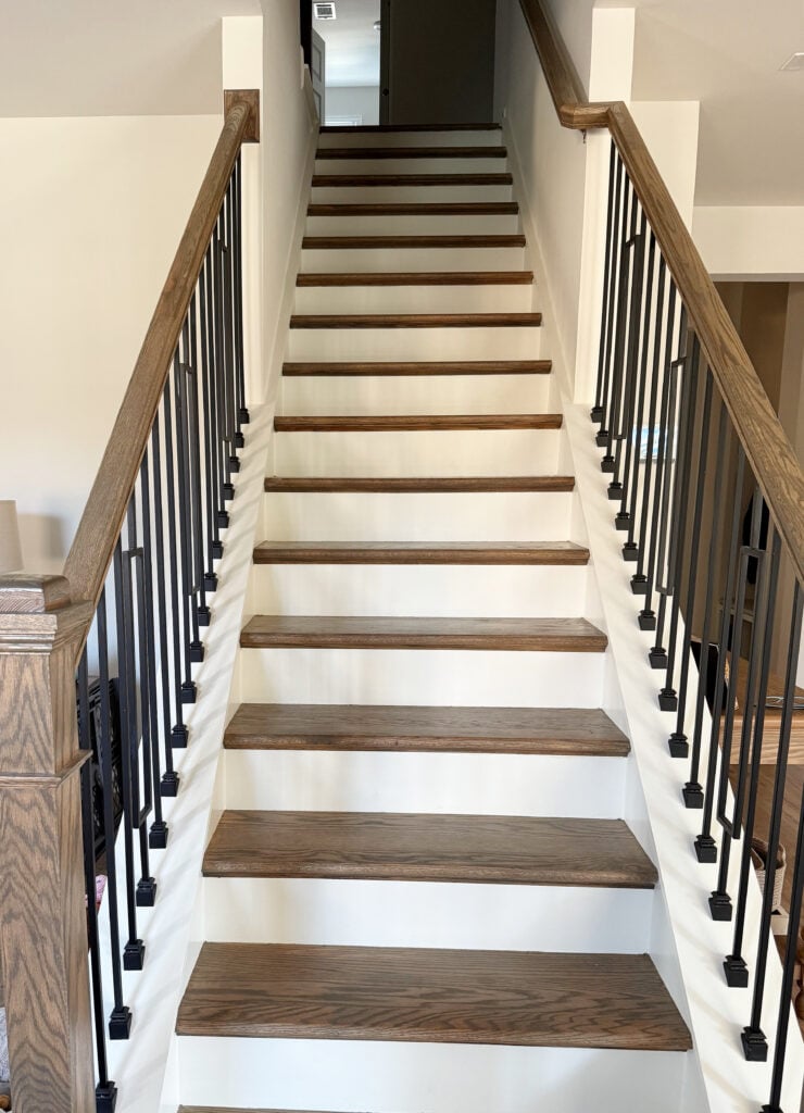 Stairs with oak dark wood treads and hand railing, metal spindles, white risers and trims. Great update ideas for 2000s staircase.