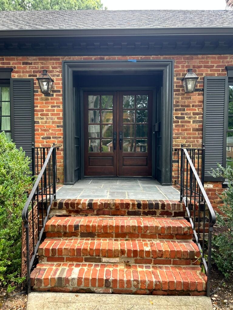 exterior with red, orange and brown brick, dark soft black painted trim, shutters, and dentil molding, double front doors in wood stain.