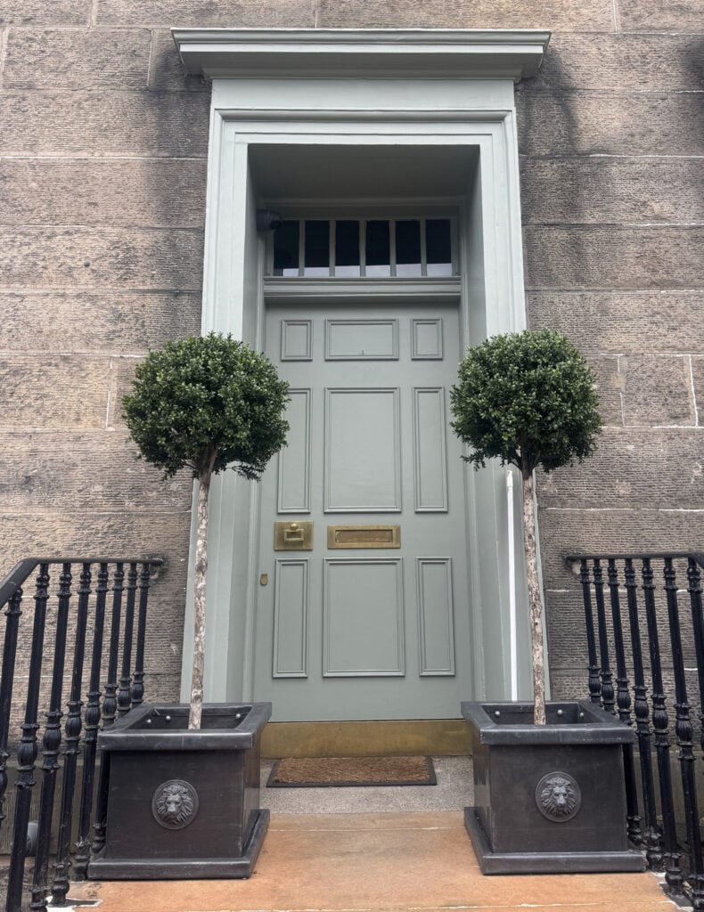 External stone on exterior of home in UK, Scotland. Front door painted a gray-green with lighter green-gray trim and orange tile steps