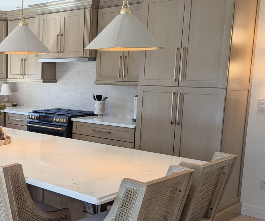 white wash wood floor and custom stained paint beige-wash wood cabinets, island, white quartz, Vicostone Misterio Gold, wood rattan stools, gold hardware, matte black oven, zellige backsplash