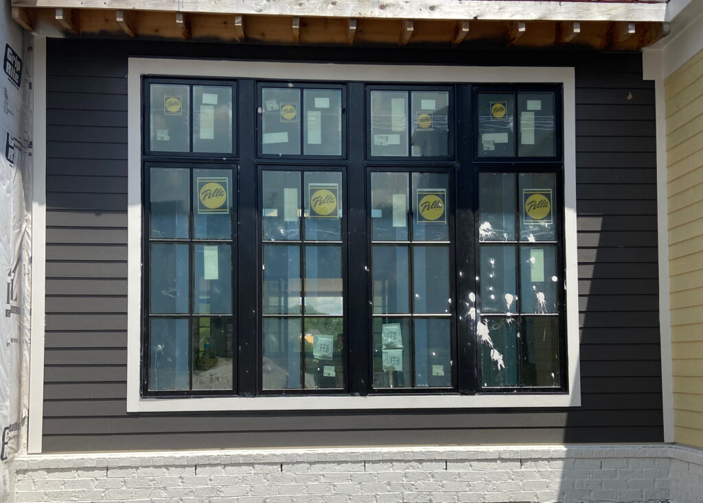 Benjamin Moore Iron Mountain on exterior siding in sun, possible south-facing, with black windows and white trim. Warm dark gray brown blend paint color