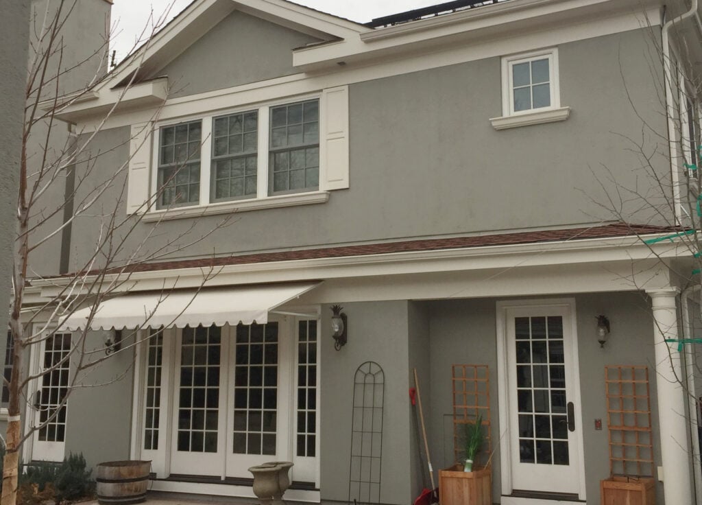 Benjamin Moore Rockport Gray painted exterior stucco on cloudy day. Shutters, trims and gutters are creamy white Sail Cloth.