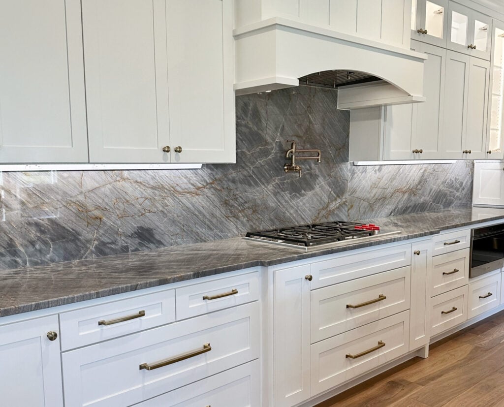 Dark Gray blue quartzite countertops, wood walnut look flooring, Sherwin Williams Pure White cabinets, glass doors on top, pot filler