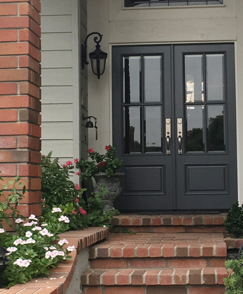 Front door paint color similar to BEnjamin Moore Cheating Heart, orange and red brick steps, porch and beam on exterior with green-gray siding, modern farmhouse 4 panel doors