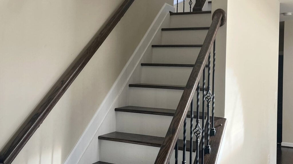 How to update a 2000 staircase, Manchester tan walls, dark wood steps, painted white riser, and wood hand railing with iron spindles