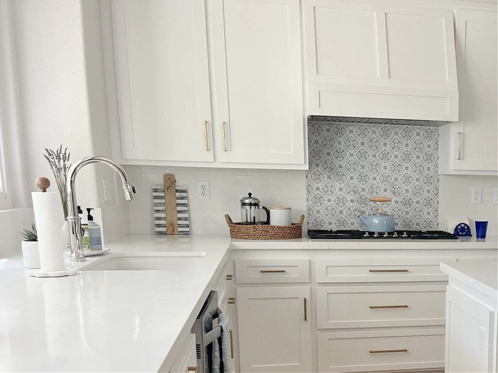 Sherwin Williams Pure White cabinets, subway tile backsplash with blue tile insert above stove, gold hardware, Classic Gray on the walls