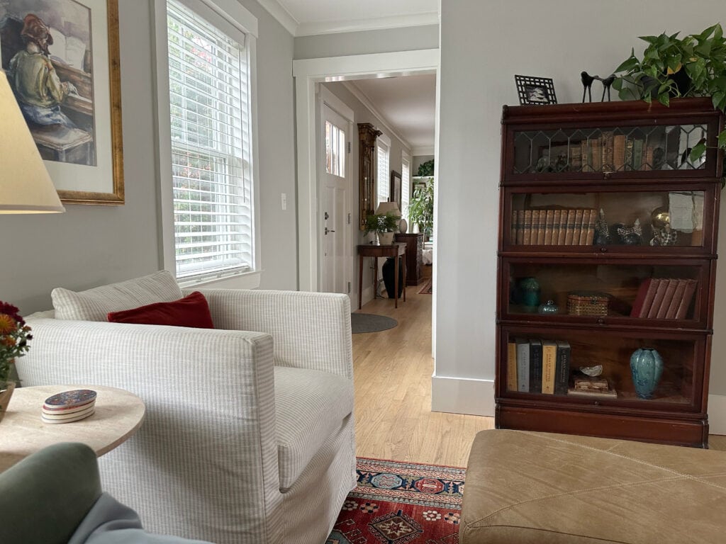 Sherwin Williams Repose Gray walls with red oak flooring and home decor, antique wood bookcase, slipcover chair. Sitting room.