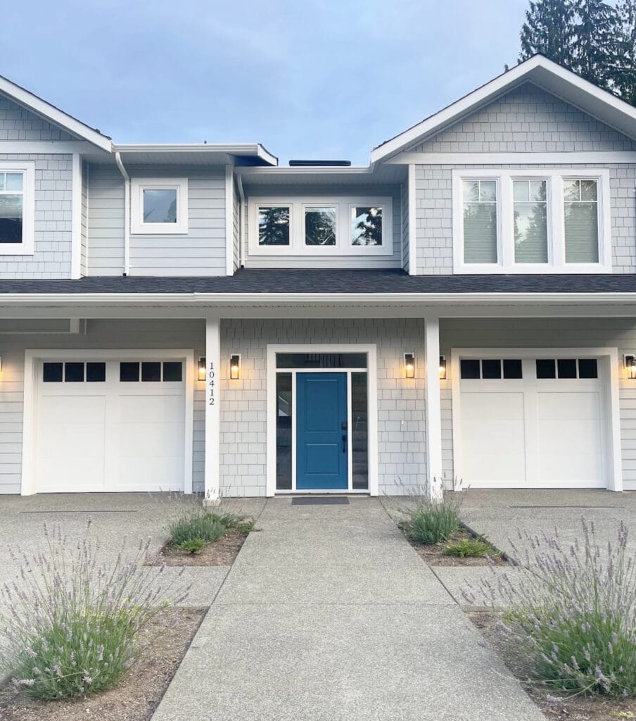 Sherwin Williams white trim, gutters, windows, and matching garage doors, Connor's Lakefront blue front door, James Hardie LIght Mist shakes and dark gray-black roof