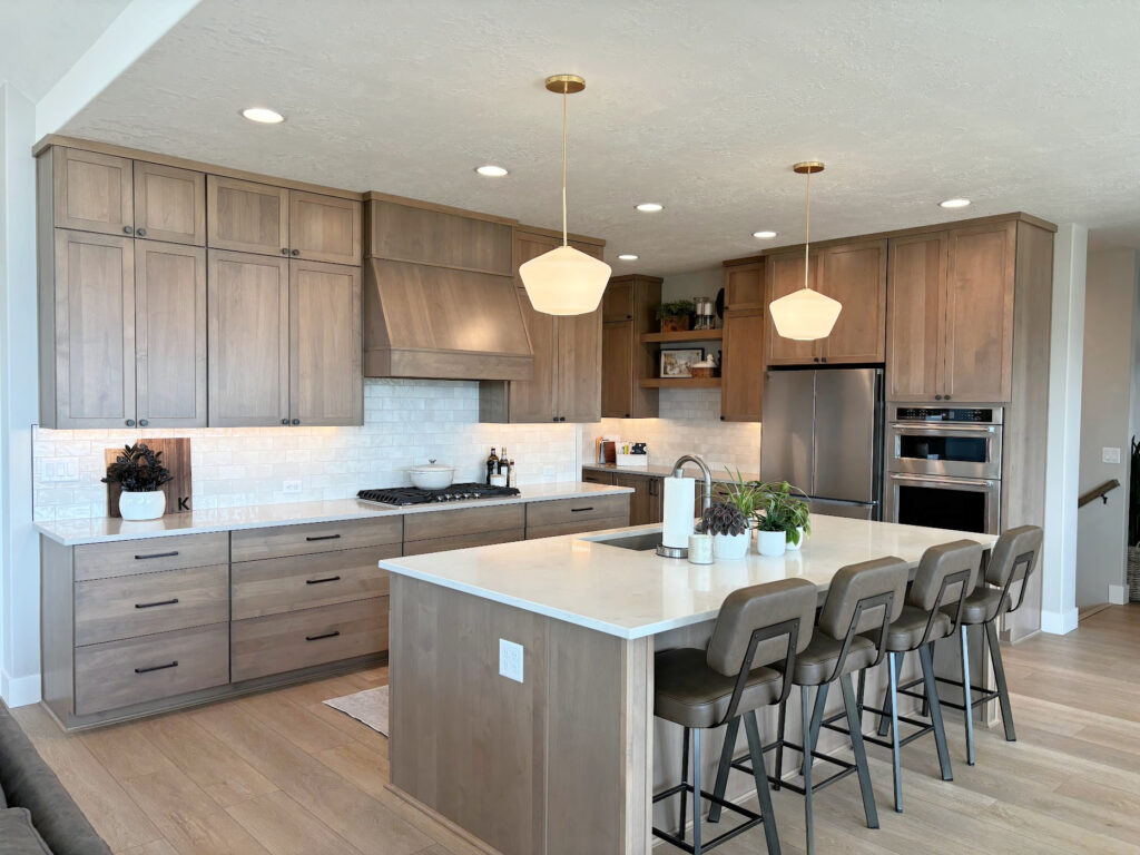 Stained wood kitchen cabinets, wood floor and island. White quartz countertop and zellige look subway tile backsplash with gold pendant lights
