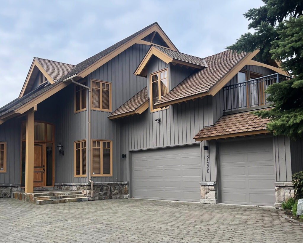 Warm gray exterior siding with cedar shake roof, trim color that looks like wood. Natural stone. Garage doors match the siding color
