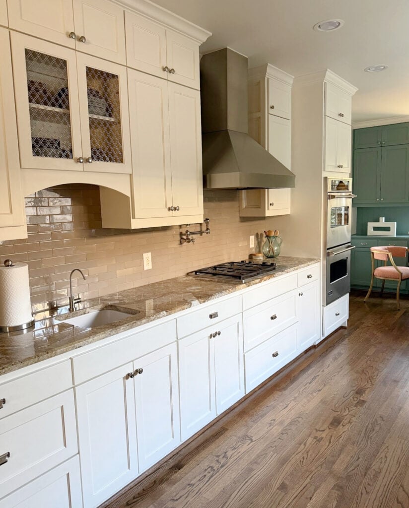 Kitchen with Sherwin Williams Dover White cream cabinets, early 2000s granite countertop, taupe subway tile backsplash and wood flooring, Underseas cabinets