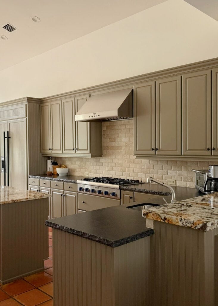 Sherwin Williams Extra White in west-facing light, greige painted kitchen cabinets, green undertone, travertine, terracotta tile floor, black granite and gold-cream island