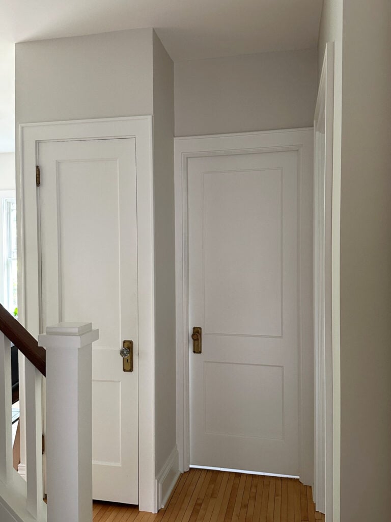 Benjamin Moore Fog Mist in hallway with Sherwin Williams Alabaster, warm white on doors, heritage strip wood flooring, natural light and dark area
