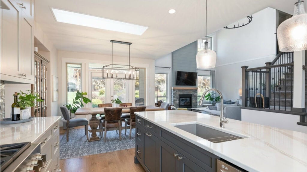 North-facing open-concept kitchen, dining room, living room, Benjamin Moore White Dove walls, darkened Revere Pewter cabinets, Urbane Bronze island, Brittanica Warm quartz countertop
