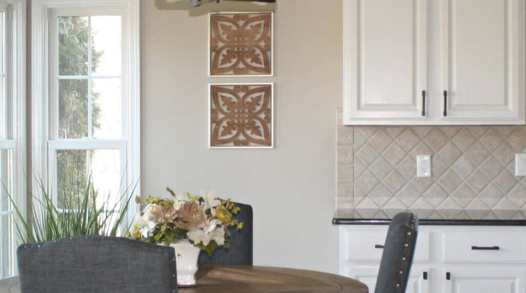 Off-white painted kitchen cabinets in 1990s kitchen, black granite, gray chairs, beige tile and walls