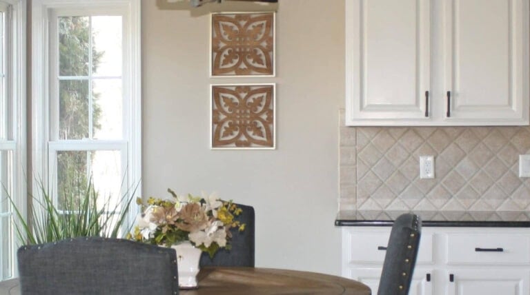 Off-white painted kitchen cabinets in 1990s kitchen, black granite, gray chairs, beige tile and walls