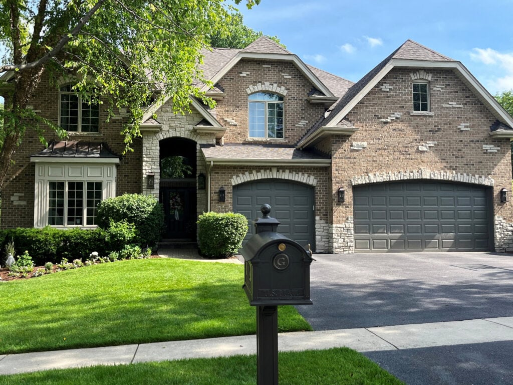 Pink beige exterior of home, South facing. Darker painted garage door in Sherwin Williams greige, stone surround trims, matching gables, taupe-greige-almond windows, asphalt roof (3)