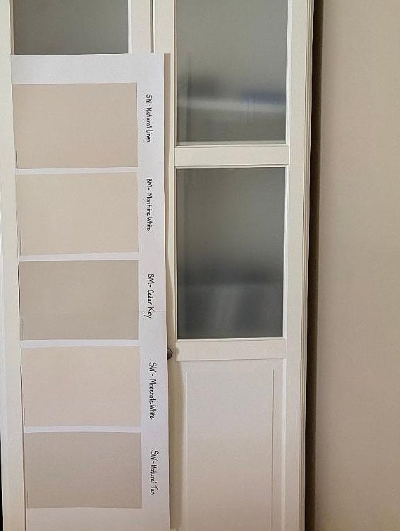 Sherwin Williams Natural Linen, Benjamin Moore Maritime White, Cedar Key, Moderate White and Natural Tan paint samples comparing wa rneutrals on a creamy cabinet